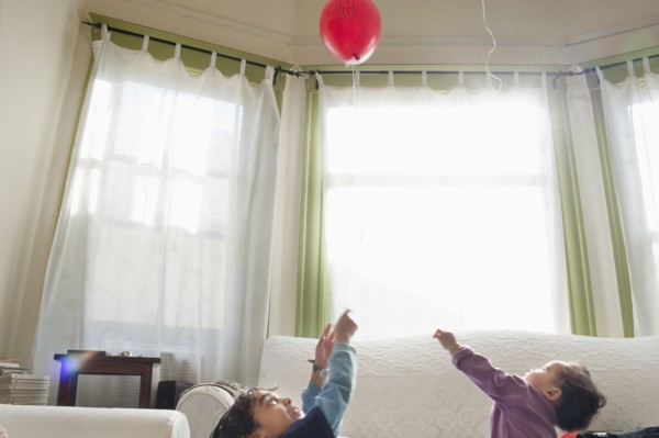 Mixed race children playing with balloon in living room