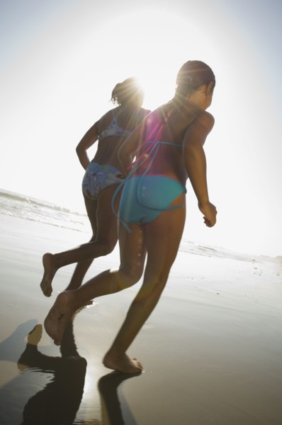 Hispanic mother and daughter running at beach