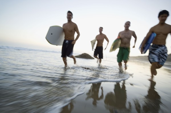 Multi-ethnic men running with surfboards