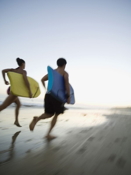 Multi-ethnic couple running with surfboards