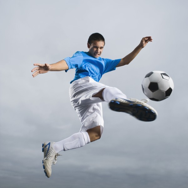 Mixed race teenager in mid-air kicking soccer ball