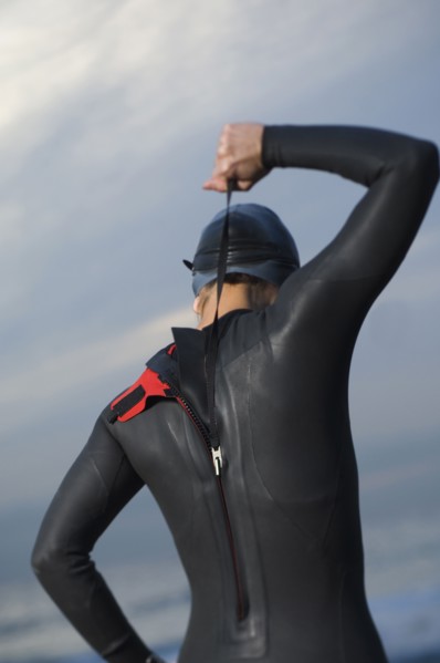 Hispanic woman zipping wetsuit on beach
