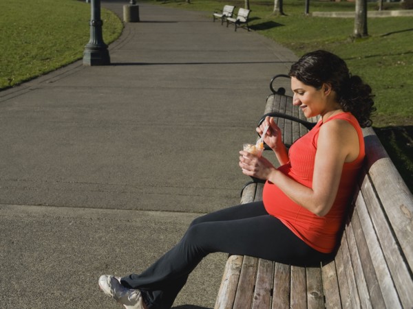 Pregnant Middle Eastern woman eating fruit in park