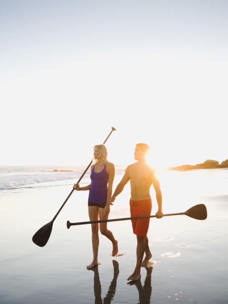 Couple walking on beach carrying paddles
