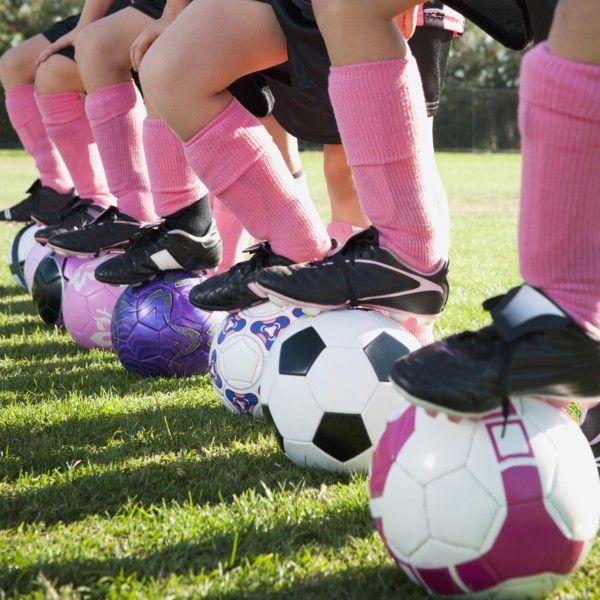 Girl soccer players standing with feet on soccer balls