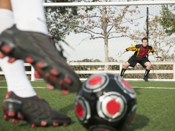 Soccer player kicking ball into goal on soccer field