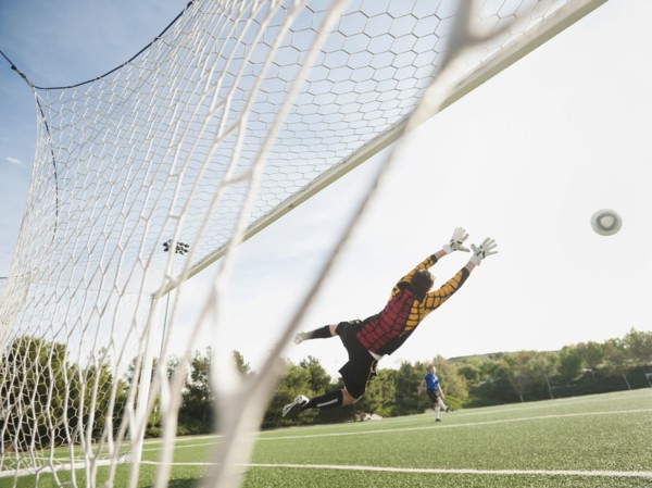 Mixed race goalkeeper in mid-air protecting goal