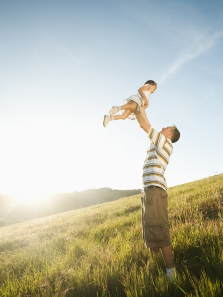 Father standing in field lifting daughter