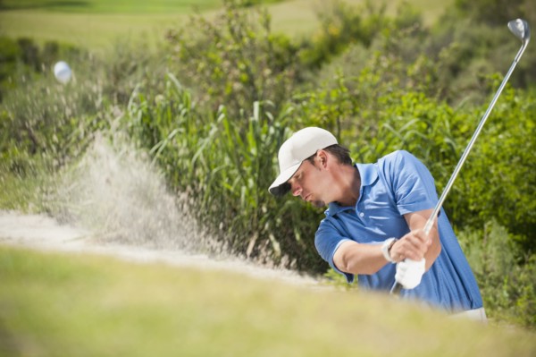Caucasian golfer hitting ball out of bunker
