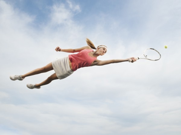 Caucasian woman jumping in mid-air playing tennis