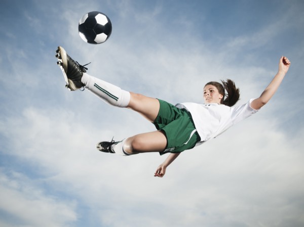 Caucasian teenager kicking soccer ball in mid-air