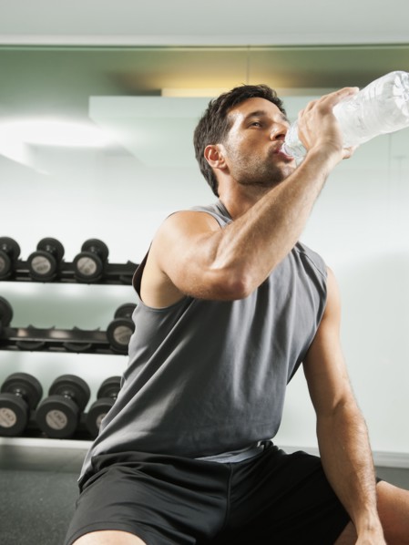 Mixed race man drinking water in gym