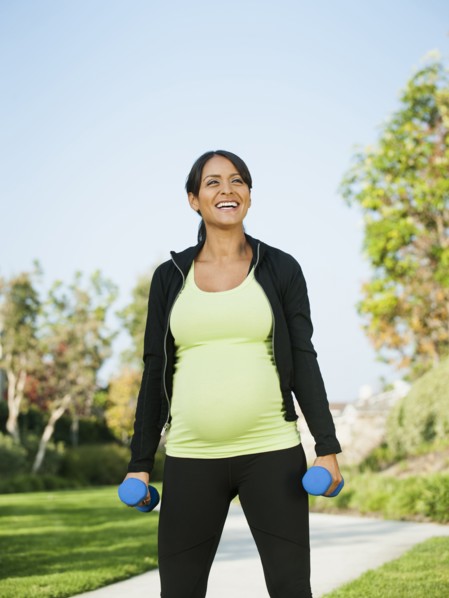 Pregnant Hispanic woman lifting weights outdoors
