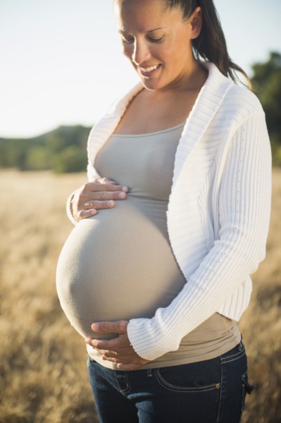 Pregnant Hispanic mother holding stomach in field
