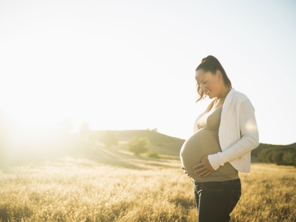 Pregnant Hispanic mother holding stomach in rural field