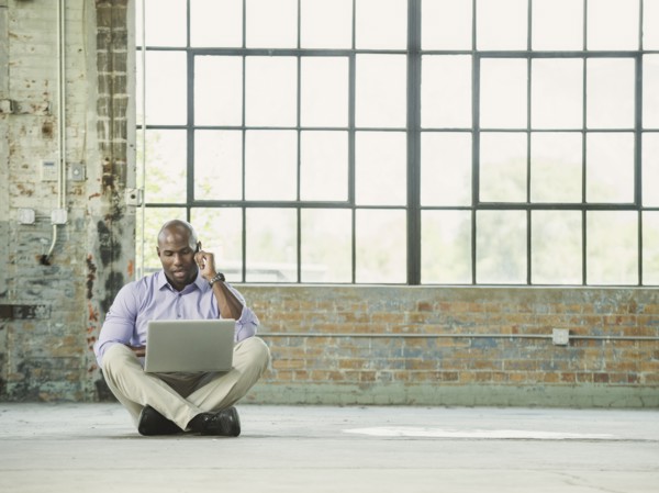 Black businessman using laptop and cell phone on warehouse floor