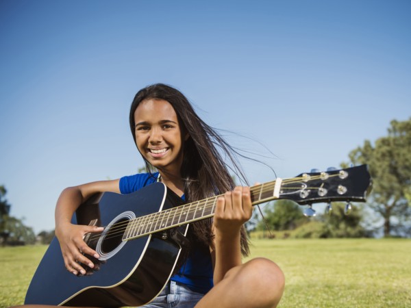 Mixed race girl playing guitar in park