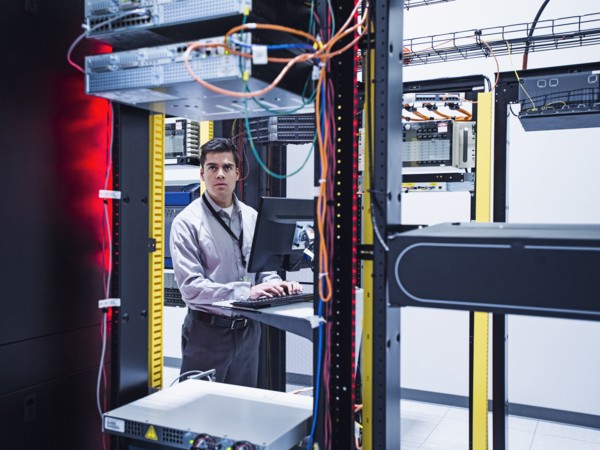 Hispanic technician using computer in server room
