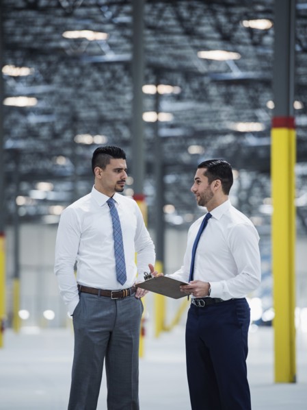 Businessmen with clipboard talking in empty warehouse