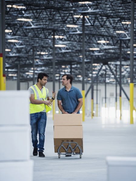Workers pushing cardboard boxes on hand truck in warehouse