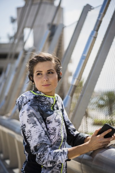 Caucasian woman leaning on bridge railing listening to earbuds