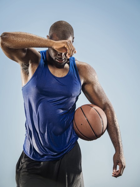 Black man holding basketball wiping sweat off forehead