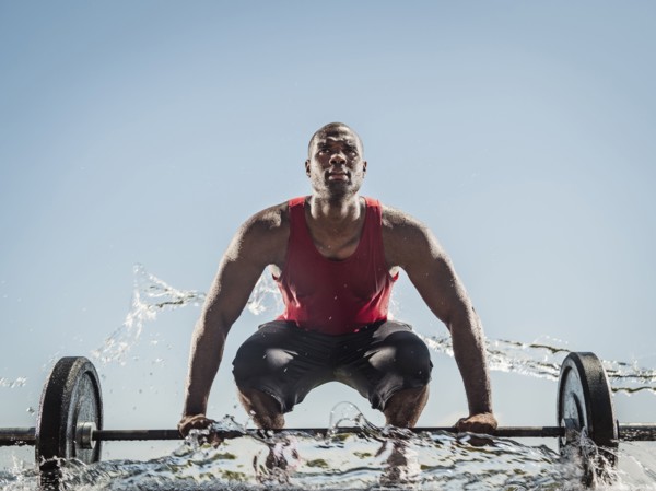 Water spraying on black man preparing for lifting barbell