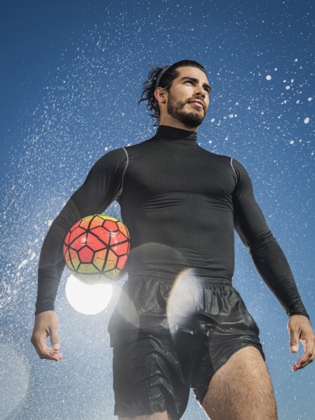 Water splashing on Hispanic man holding soccer ball