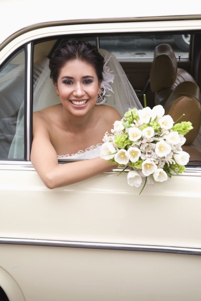 Hispanic bride sitting with bouquet in back of car