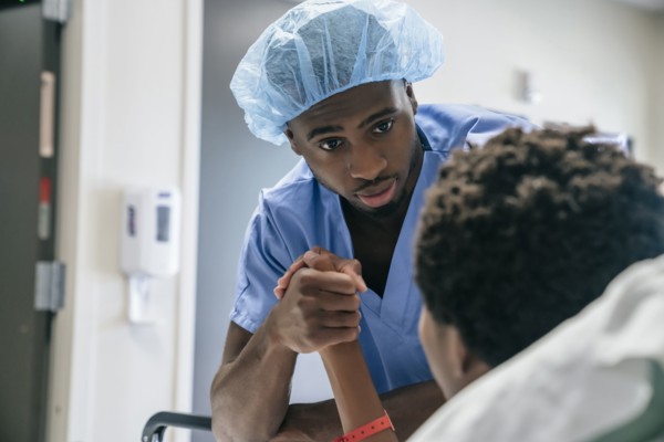 Black doctor holding hand of boy in hospital bed