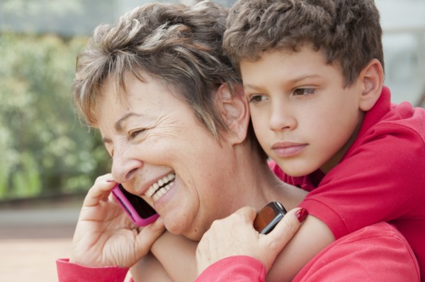 Hispanic boy hugging grandmother talking on cell phone