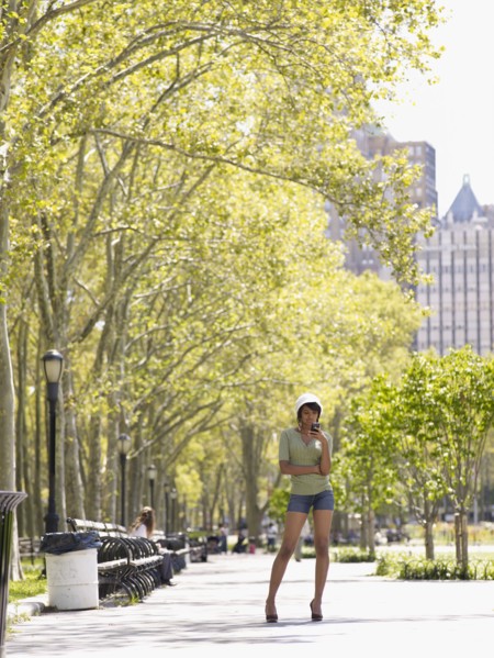 Hispanic woman text messaging on cell phone in park