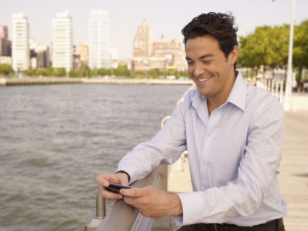 Man at waterfront text messaging on cell phone
