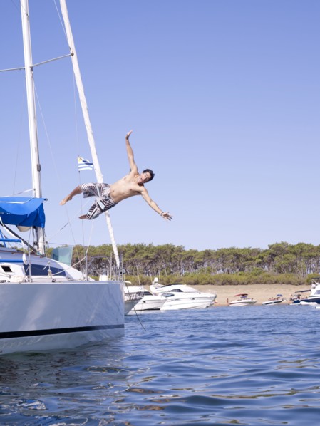 Hispanic man jumping into ocean from sailboat