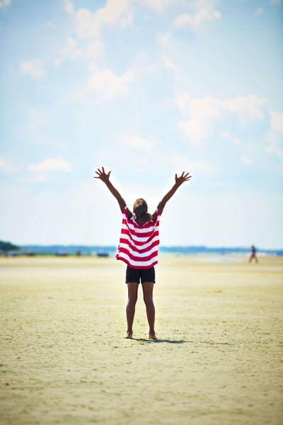 Black girl standing with arms raised on beach