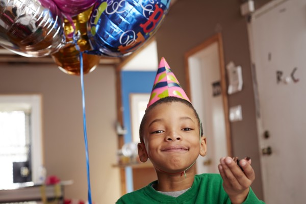 Black boy wearing party hat holding balloons