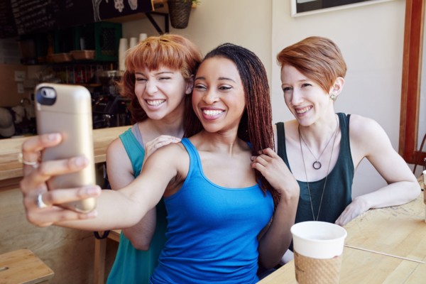 Smiling women posing for cell phone selfie in coffee shop