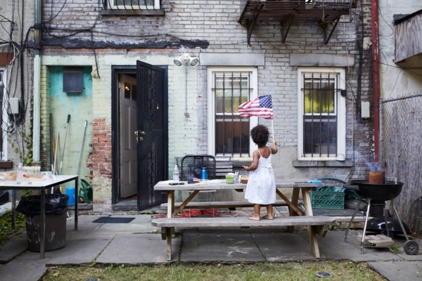 Mixed Race girl standing on backyard bench waving American flag