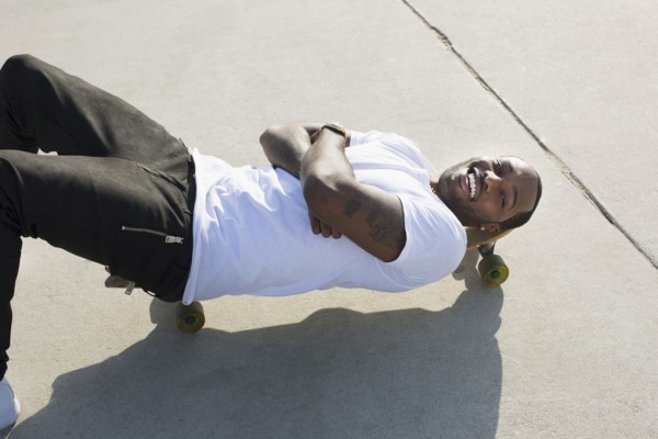 African American man laying on skateboard on city street