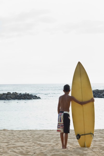 Mixed race boy on beach with surfboard