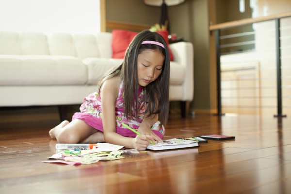 Mixed race girl writing in book on floor