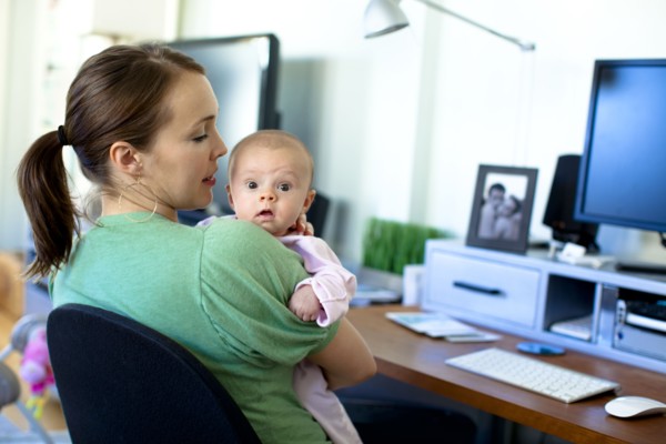 Caucasian mother working in home office and holding baby
