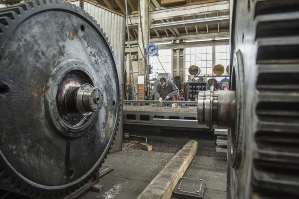 Caucasian man working behind metal cogs in metal shop