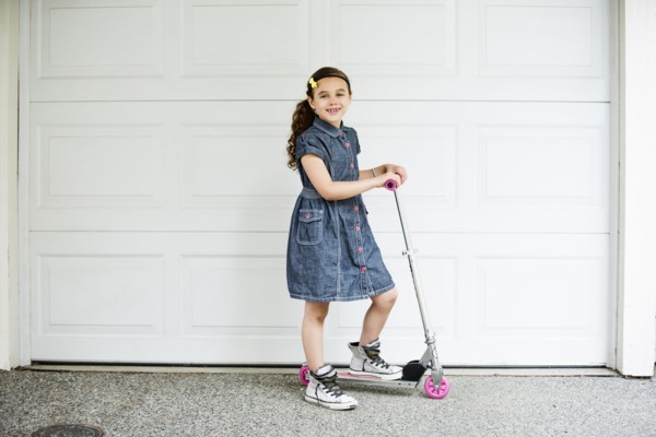 Mixed race girl smiling on scooter in driveway