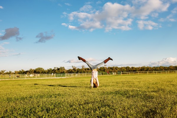 Caucasian girl doing headstand in field on ranch