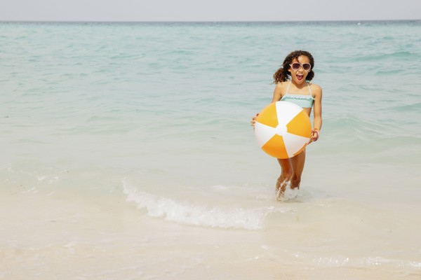 Mixed race girl holding beach ball in ocean waves