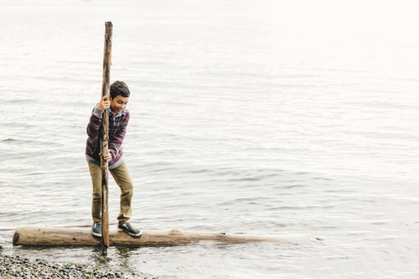 Mixed race boy playing on log in lake
