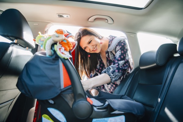 Hispanic mother fastening car seat in car