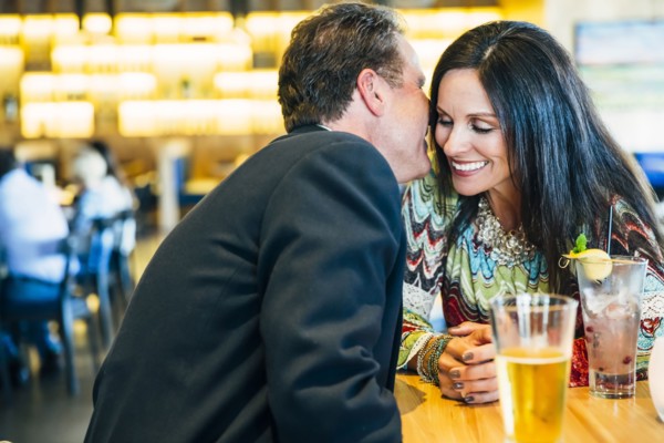 Caucasian man whispering to ear of woman in restaurant