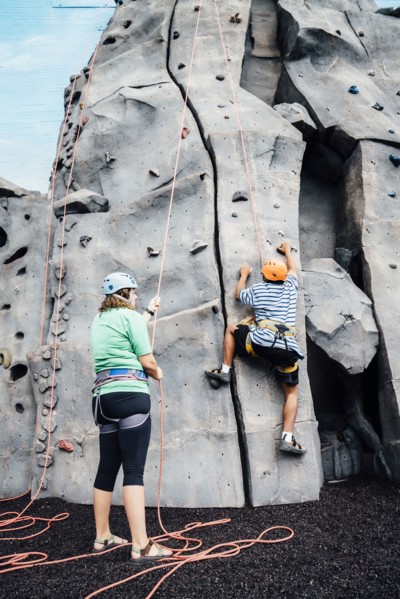 Woman holding rope for man climbing rock climbing wall